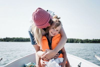 Mother hugging happy daughter whilst on a boat in summer in sweden
