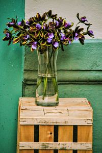 Flowers in vase on wooden crate against wall