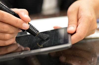 Close-up of person cleaning digital tablet on table 