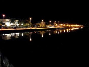 Illuminated city by river against sky at night