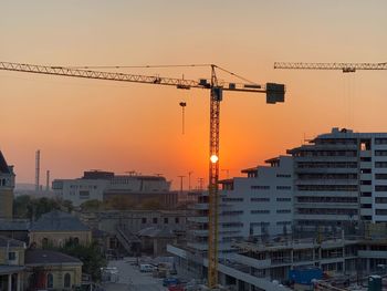 Cranes in city against sky during sunset