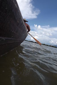 Low angle view of man in boat on river against cloudy sky