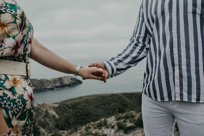Midsection of couple holding hands against sky