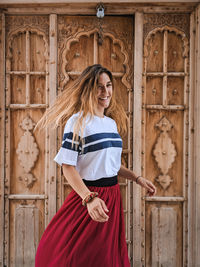 Portrait of a smiling young woman standing against door