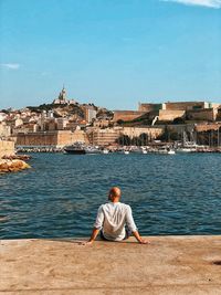 Rear view of man sitting by sea against sky