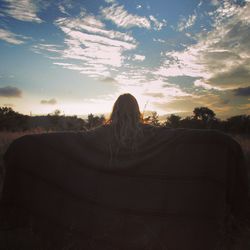 Rear view of woman sitting on landscape against sky