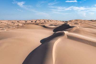 Large sand dunes with texture, patterns, light and shadow. blue sky with white clouds.