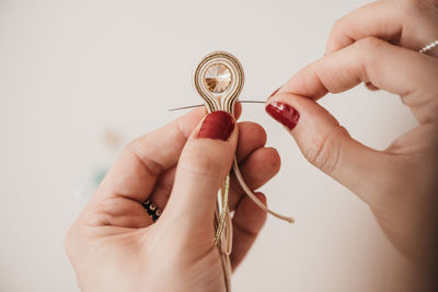 Closeup of unrecognizable female artisan with thread and needle creating handmade soutache decorations in studio