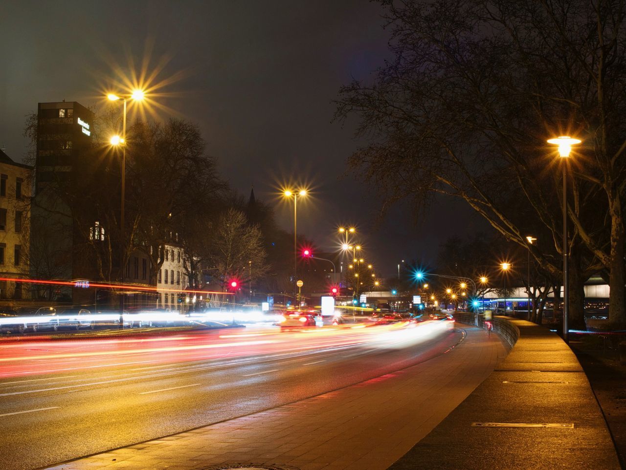 LIGHT TRAILS ON ROAD ALONG ILLUMINATED STREET LIGHTS AT NIGHT