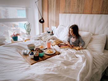 Midsection of little girl sitting on bed having breakfast 