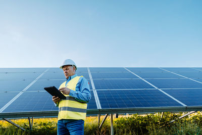 Elderly engineer is checking with tablet an operation of sun and cleanliness on field