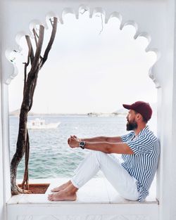 Side view of man sitting by sea against sky