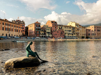 View of buildings by river against cloudy sky