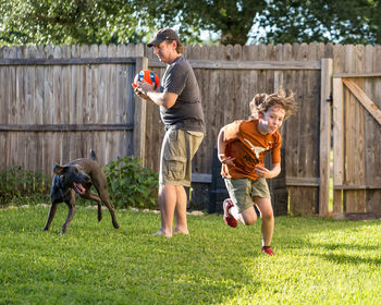 Father and son playing with dog on grassy land in yard