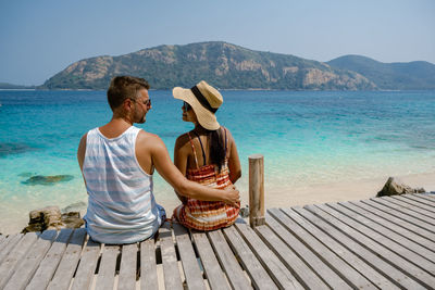 Rear view of couple sitting on shore against sky