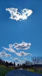 Road by trees on field against blue sky