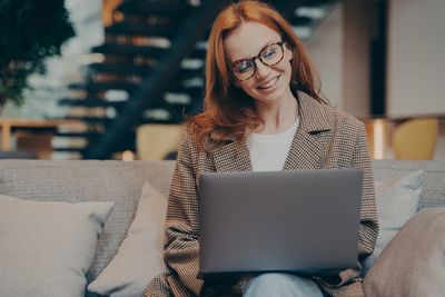 Young woman using laptop while sitting on sofa at home
