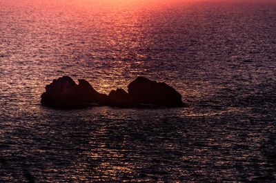 Rock formation in sea against sky during sunset