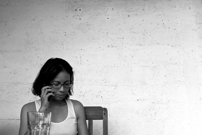 Young woman talking on mobile phone while sitting against wall