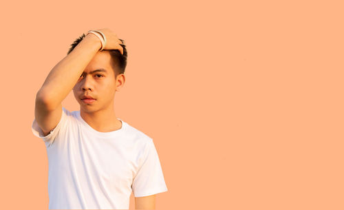Portrait of young man looking away against orange background