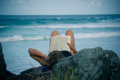 Close-up of woman reading book in sea against sky