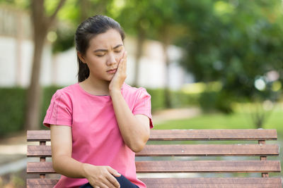 Young woman suffering from toothache sitting on bench at park