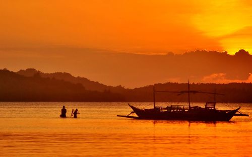 Silhouette boats in sea against orange sky