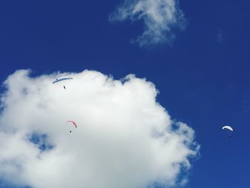 Low angle view of people paragliding against blue sky