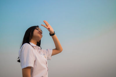 Low angle view of young woman shielding eyes standing against sky during sunset