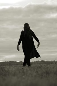 Rear view of woman walking on field against sky