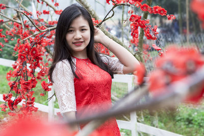 Portrait of young woman standing amidst red flowers