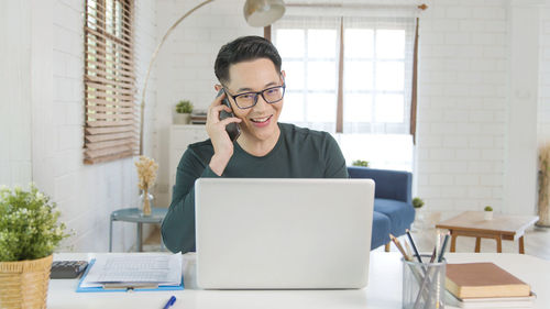 Young man using phone while sitting on table