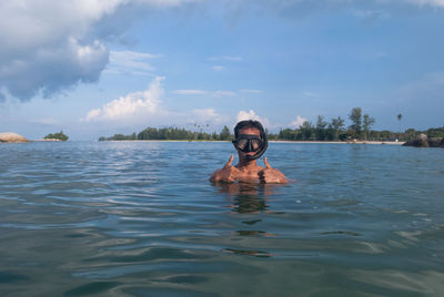 Man with swimming goggles in river showing thumbs up sign against sky