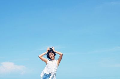 Low angle view of woman standing against blue sky