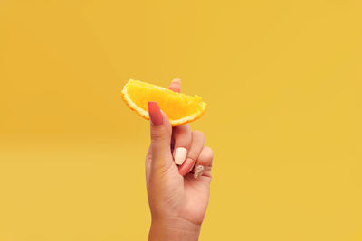 Close-up of hand holding orange fruit against yellow background