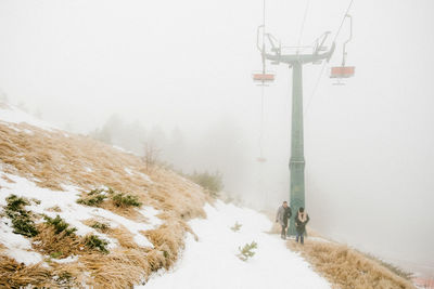 Low angle view of ski lift against clear sky with people walking 