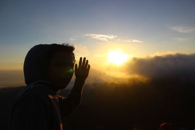 Man shielding eyes against sky during sunrise