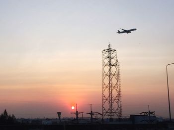 Low angle view of silhouette communications tower and airplane against sky during sunset