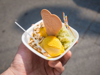 Close-up of hand holding mango ice cream with sticky rice and peanuts on chatuchak weekend market, bangkok, thailand