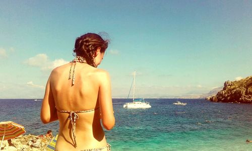 Rear view of woman at beach against sky during sunny day