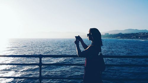 Silhouette of woman standing by railing against sea