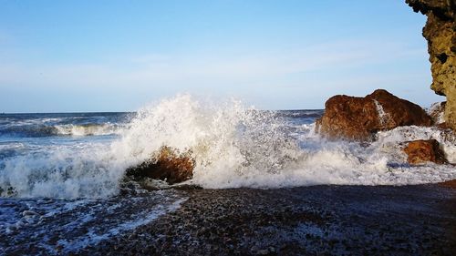 Waves breaking on rocks at beach against sky