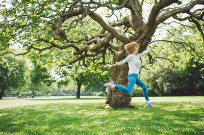 Side view of happy woman with arms raised jumping in park