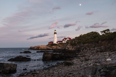 Lighthouse by sea and buildings against sky