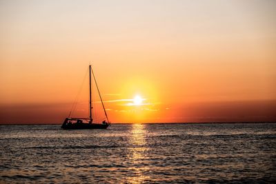 Silhouette sailboat sailing on sea against sky during sunset