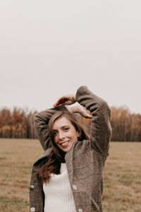 Portrait of smiling young woman standing on field against sky during winter