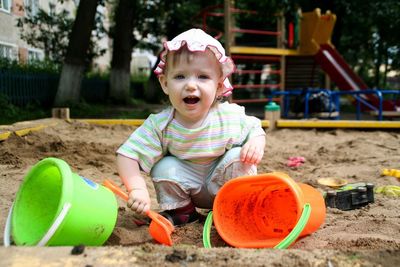 Portrait of cute happy girl playing with sand pail and shovel in sand