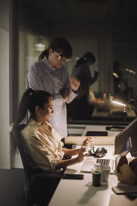 Businesswoman discussing with female colleague over laptop while working late in office