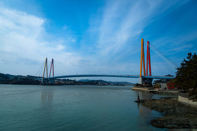 View of suspension bridge over river against cloudy sky