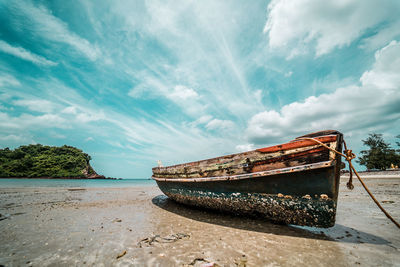 Abandoned boat moored on beach against sky